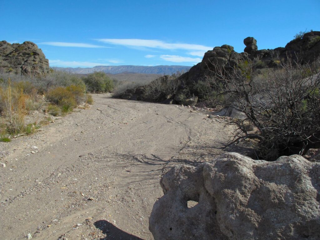 A dry stream bed filled with sand and gravel.