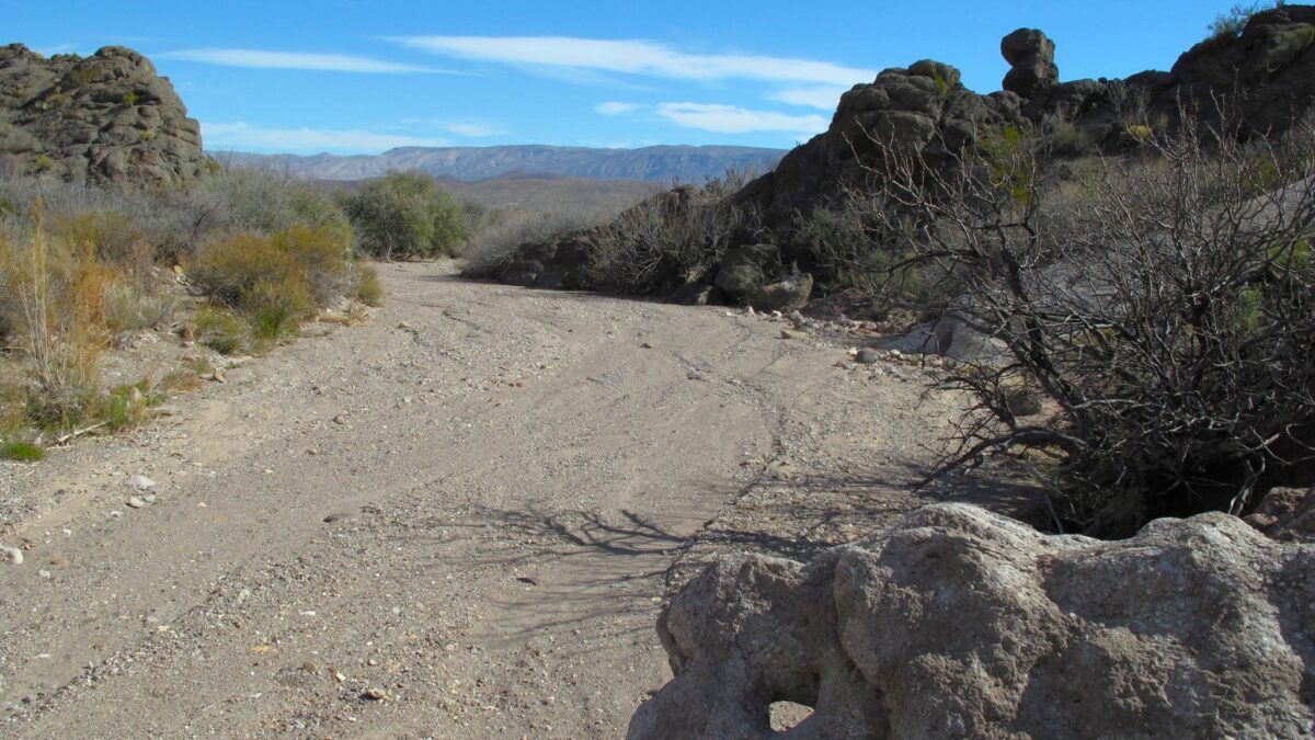 A dry stream bed filled with sand and gravel.