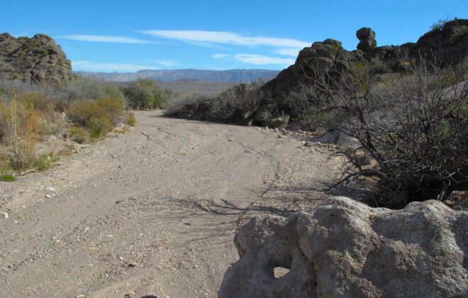 A dry stream bed filled with sand and gravel.
